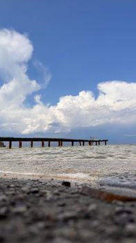 Peaceful beach scene with a wooden pier and fluffy clouds above the shoreline, evoking tranquility.