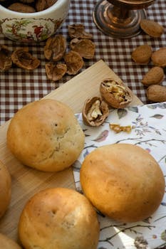 Freshly baked bread rolls with walnuts and almonds on a checkered tablecloth, sunlight streaming.