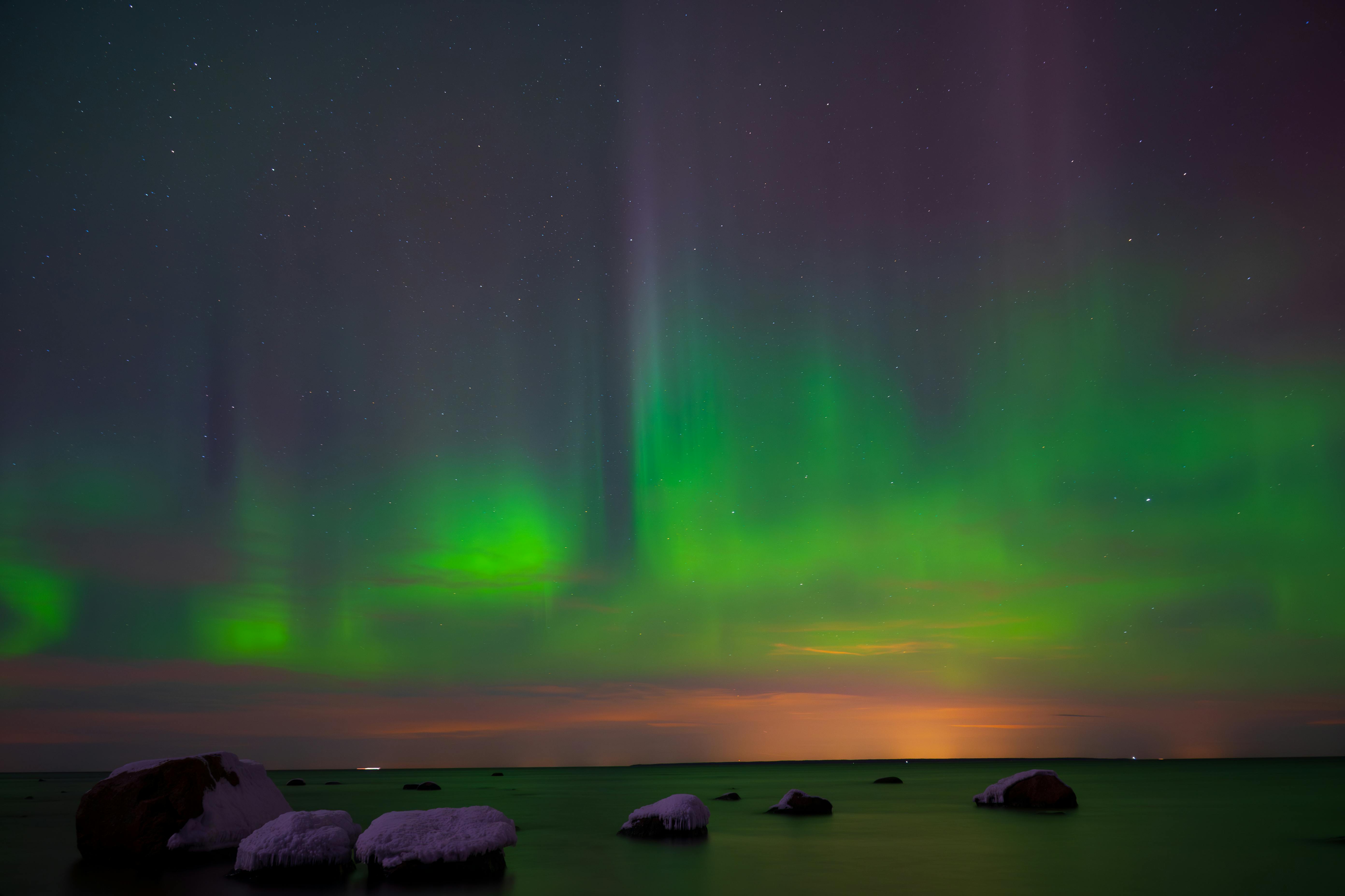 Capture of vivid Northern Lights reflecting over the serene Estonian coastline.