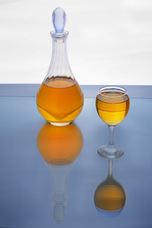 Free A glass decanter and wine glass filled with golden liquid on a reflective blue surface, creating an artistic ambiance. Stock Photo