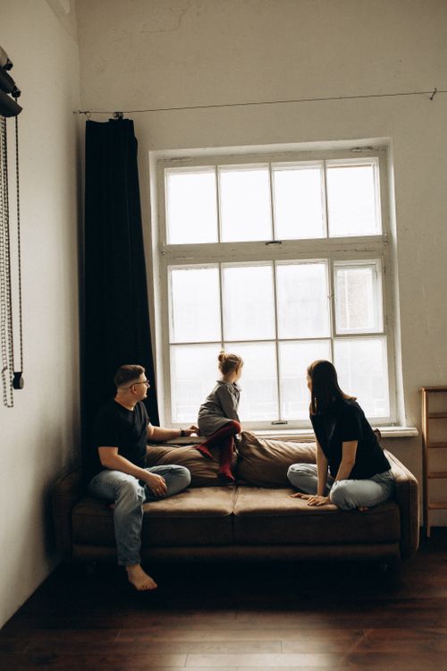 Free Casual family scene by a large window on a cozy couch, capturing a moment of leisure. Stock Photo