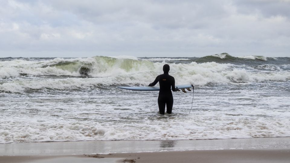 Surfer in wetsuit stands ready to tackle the Baltic waves at Jastrzębia Góra's beach in Poland.