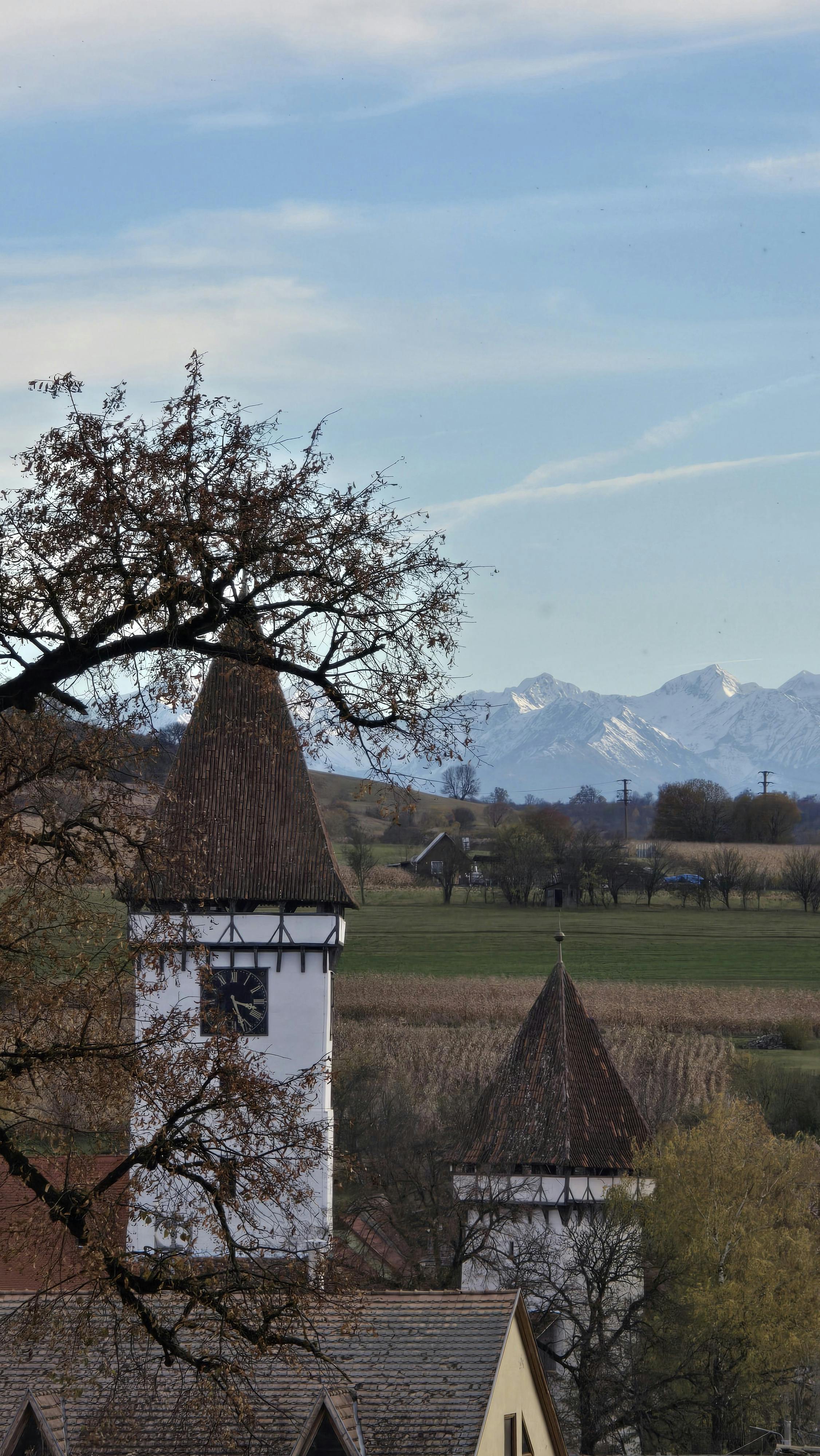 Picturesque village scene featuring towers with mountains under a blue sky. Captivating and serene.