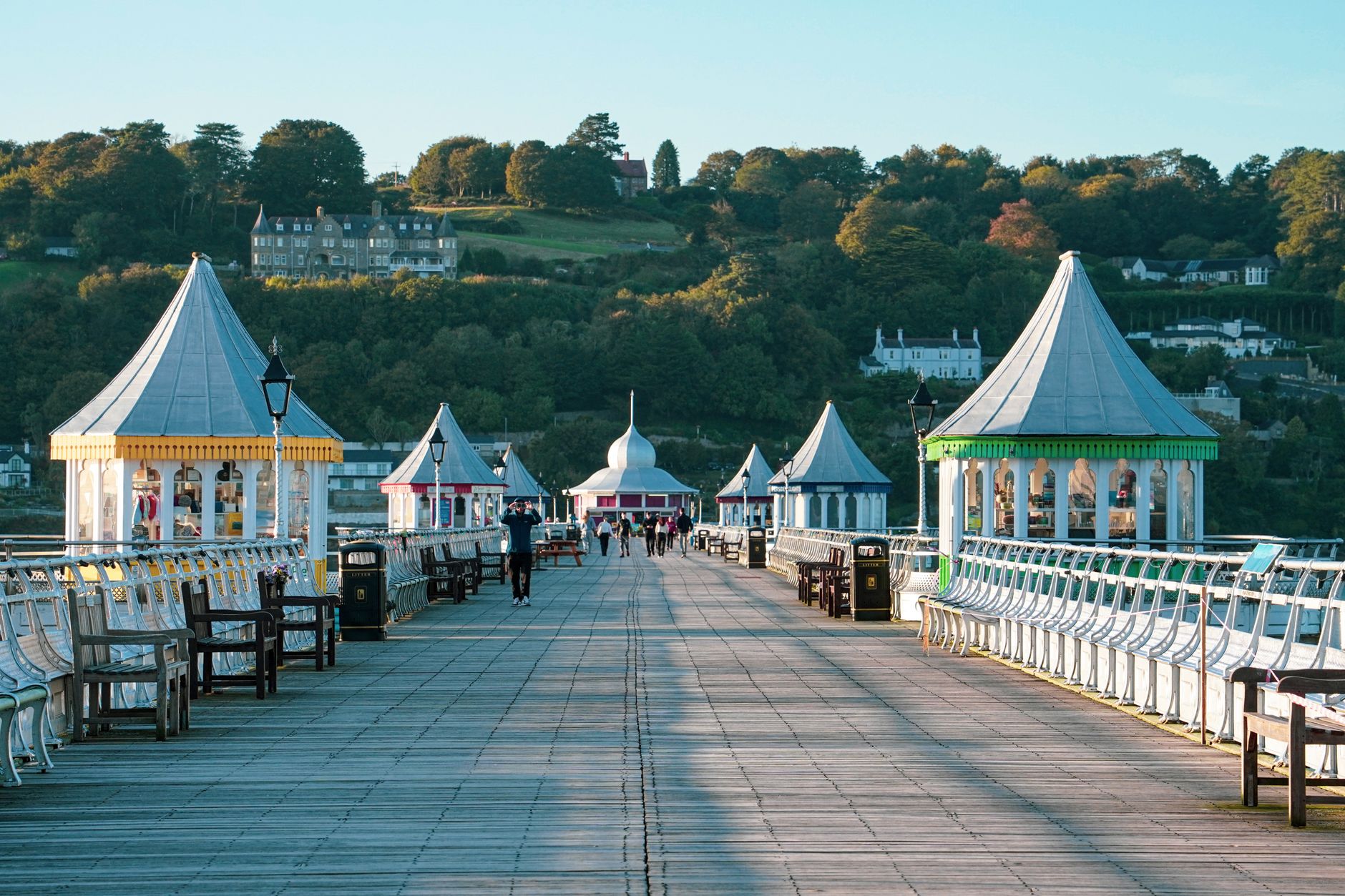 Charming view of Bangor Pier in Wales, showcasing vibrant kiosks and lush greenery.