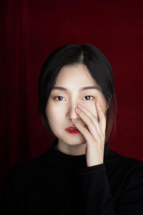 Free Portrait of a woman in a black top with a red background, showcasing a thoughtful expression. Stock Photo