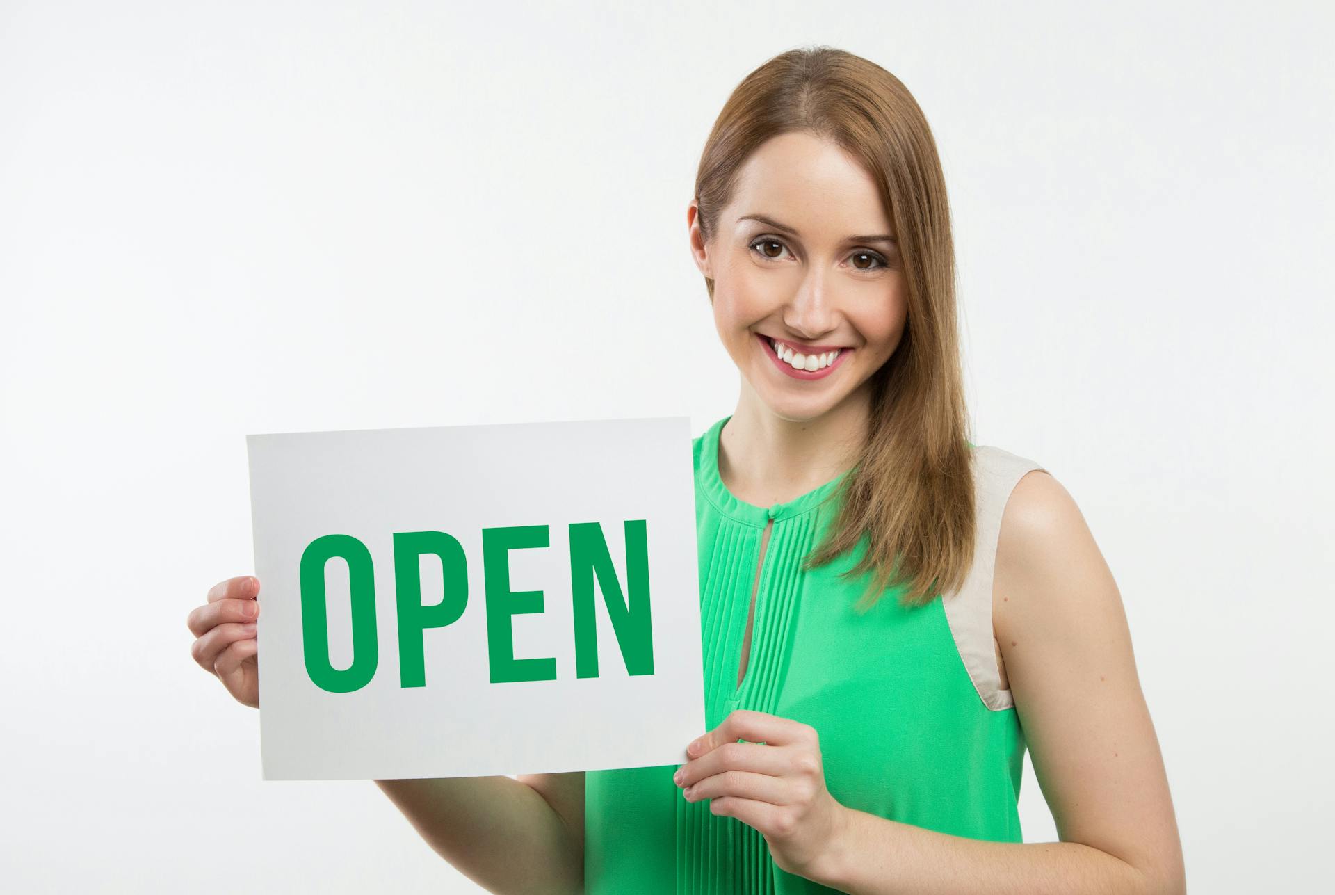 Cheerful woman in green holding an open sign, perfect for business use.