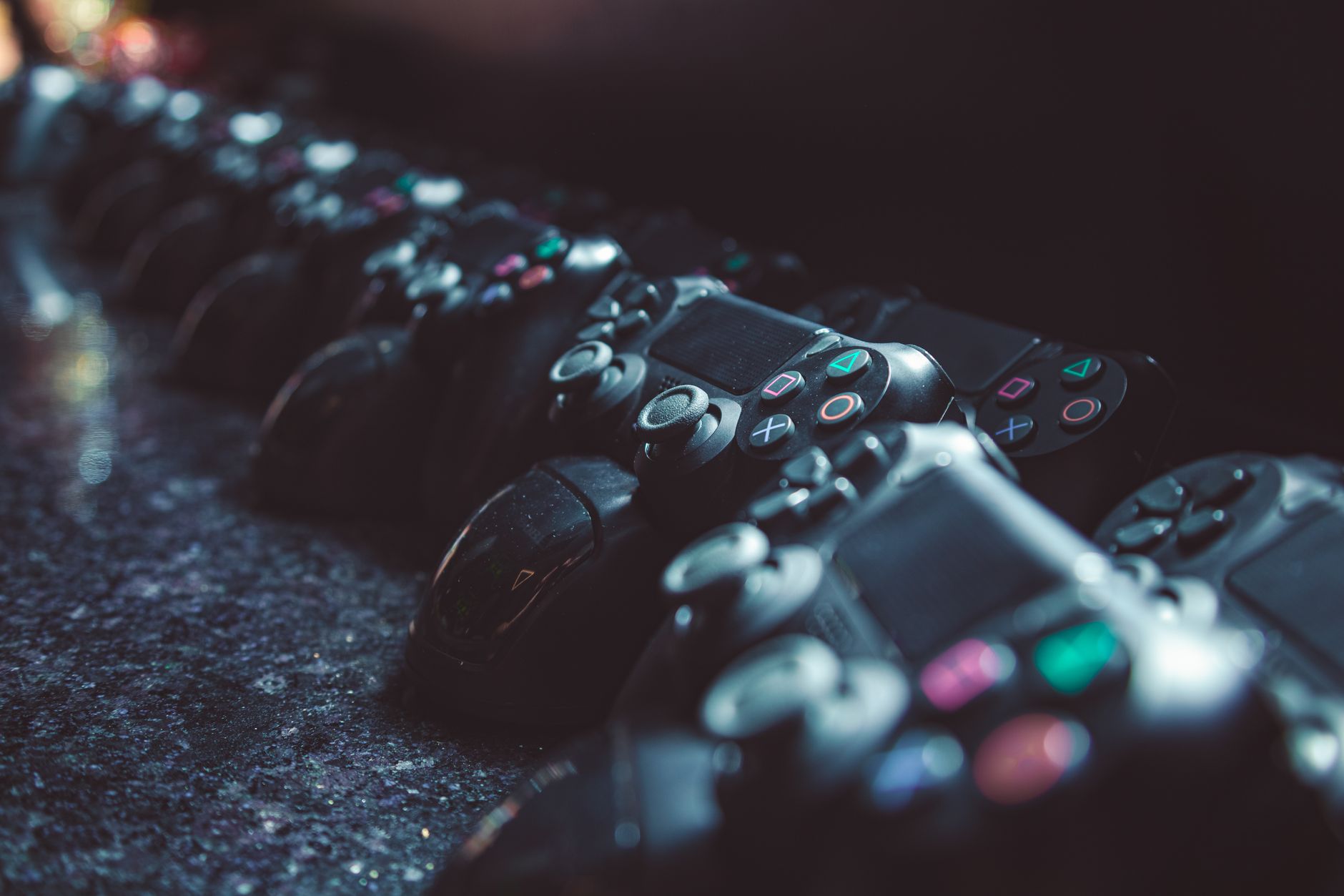 Series of gaming controllers lined up on a reflective surface, dimly lit.