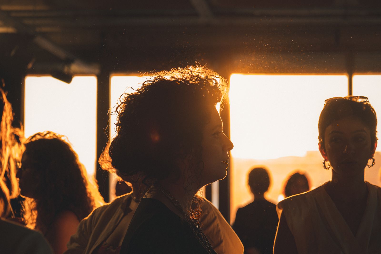 Woman with curly hair in profile, backlit by golden sunset light through large windows indoors