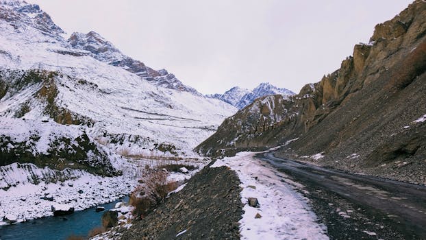 Scenic view of a winding mountain road surrounded by snowy peaks and a clear river.