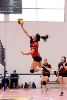 Woman volleyball player performing a jump spike during an indoor match with teammates and spectators.