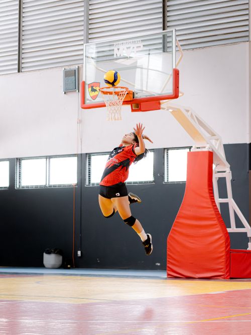 Free Athlete in red and black uniform jumps to spike the volleyball through a basketball hoop. Stock Photo