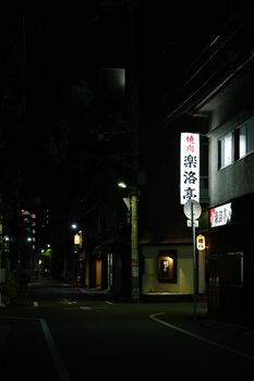 A tranquil night scene of a Japanese street with illuminated neon signs and empty sidewalks.
