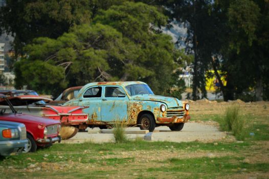 Rusty vintage car in an outdoor setting in Antalya, Türkiye, with greenery background.