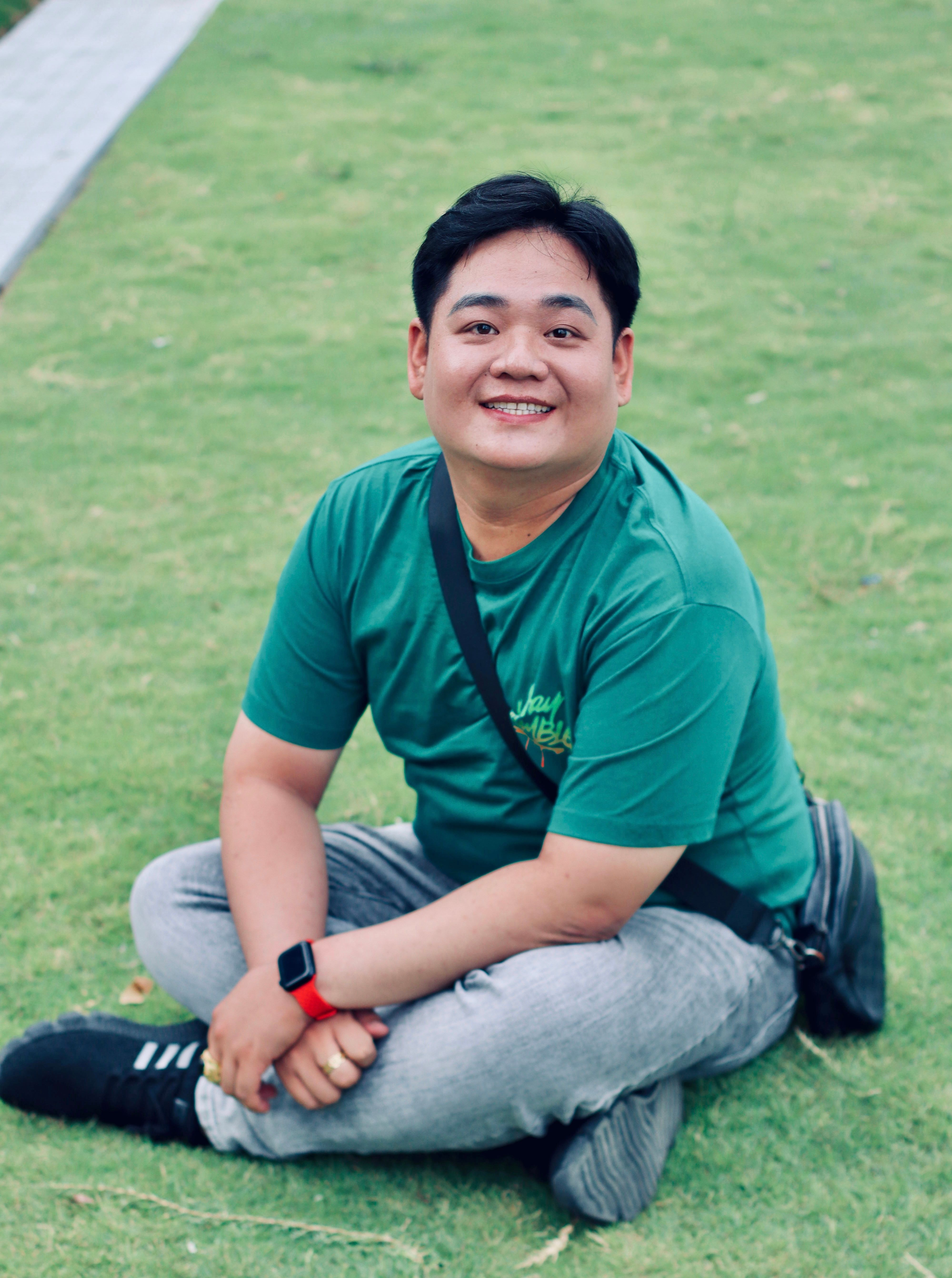 A cheerful man sitting cross-legged on grass, enjoying outdoor leisure.