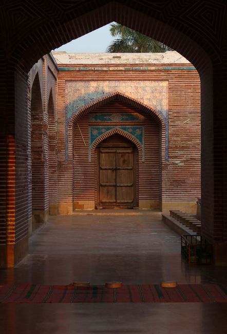 Explore the intricate architecture of a historical mosque courtyard featuring archways and a wooden door.