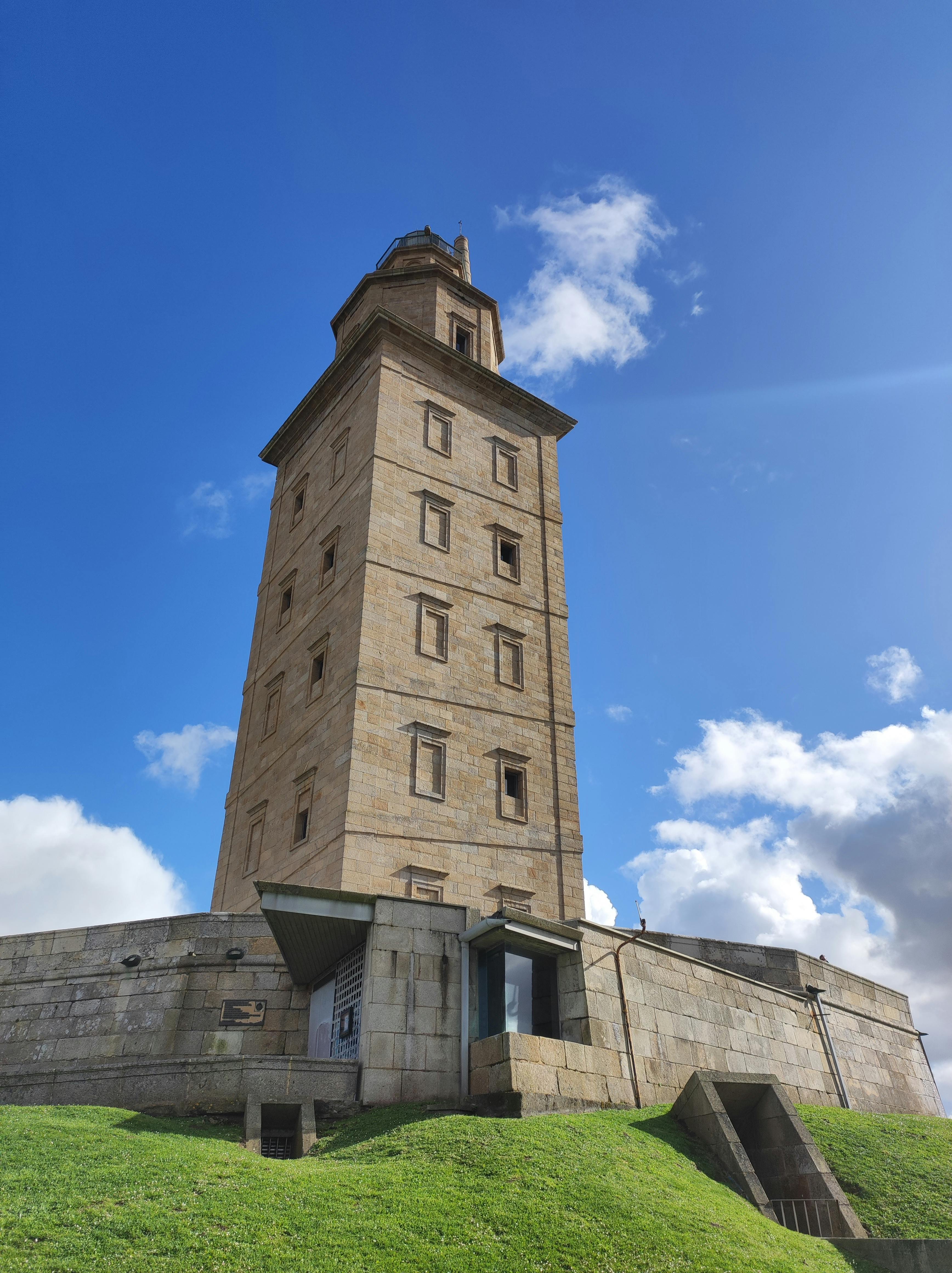 View of the Tower of Hercules under a bright blue sky, showcasing ancient Roman architecture.