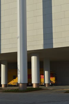 Architectural shot of a modern building with white pillars and a yellow truck. Urban scene.