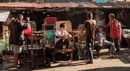 Free Action-filled street market scene featuring vendors and carts under rustic metal roofing. Stock Photo