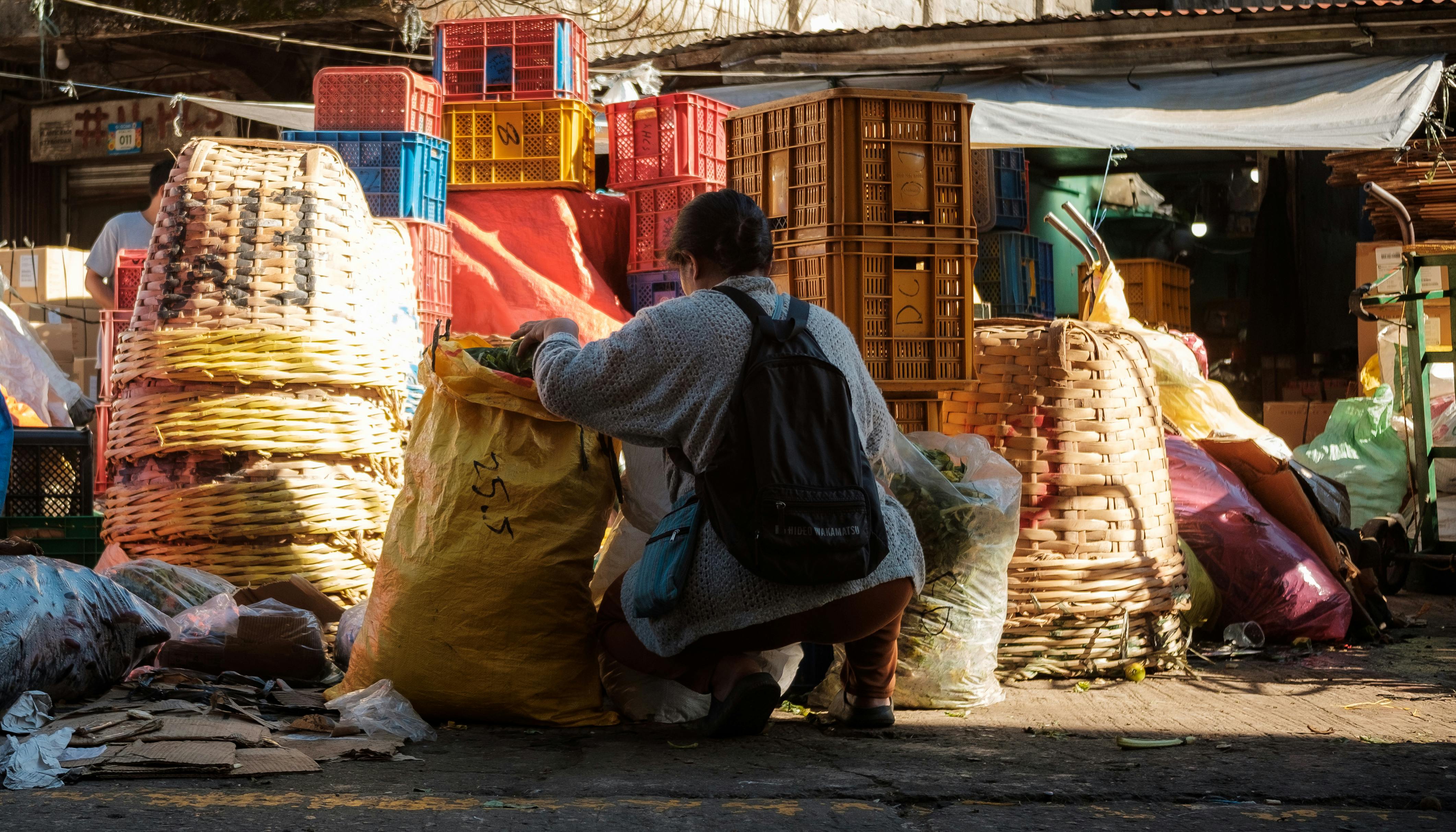 Individual organizing recyclables at a bustling outdoor market with colorful crates and baskets.