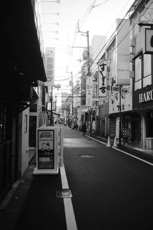 Free Black and white photograph of a quiet urban street in Japan with vintage signage and narrow alleys. Stock Photo