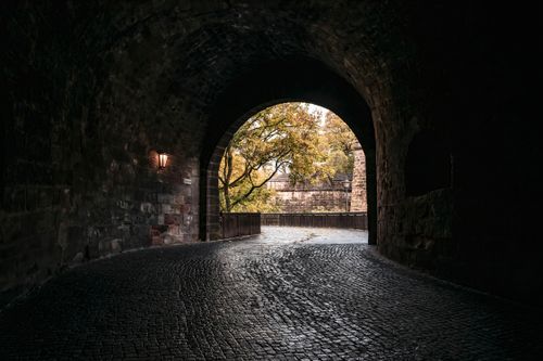 Free Atmospheric view from a historic tunnel in Nuremberg revealing trees and cobblestones. Stock Photo