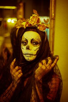 Portrait of a person with intricate Dia de los Muertos makeup and floral headpiece.