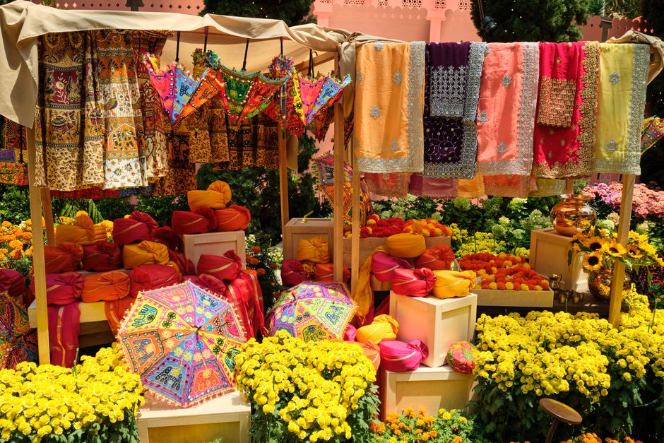 Colorful Indian textiles and flowers on display at an outdoor market, showcasing cultural vibrancy.