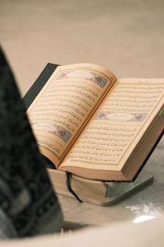 An open Quran displayed on a traditional stand, featuring intricate Arabic calligraphy.