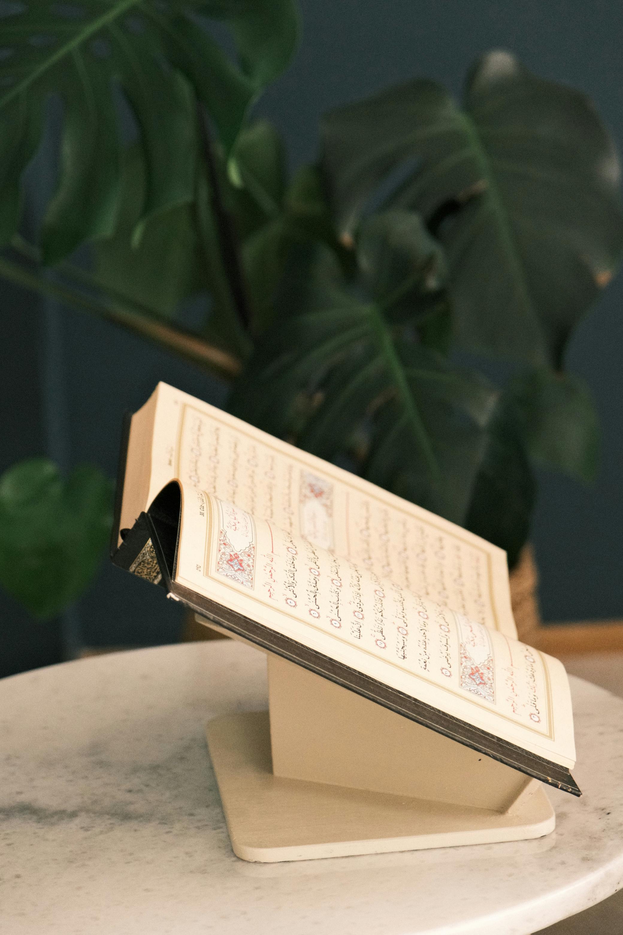 Gratis Libro religioso aperto su un supporto in marmo con foglie tropicali, che crea un'atmosfera serena. Foto a disposizione