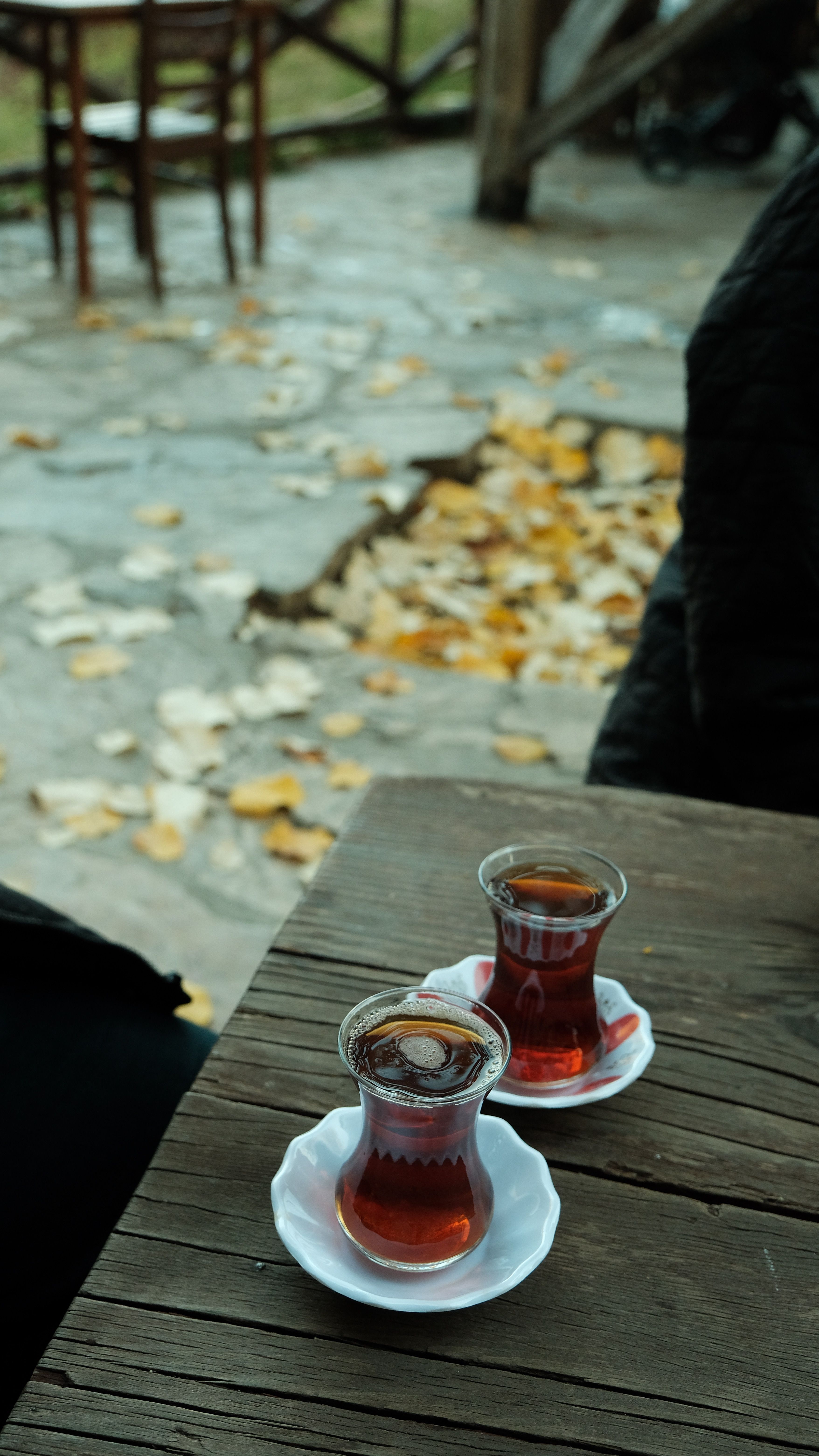 Two glasses of tea on a rustic table outdoors with autumn leaves.