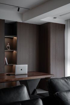 Sleek home office with dark wood decor, leather sofa, and laptop on a table.