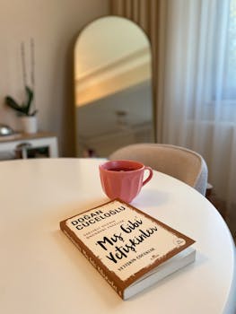 A tranquil indoor scene with a book and red coffee mug on a round table.