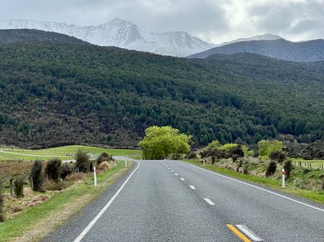Picturesque road leading through lush forests and snowy mountains in Southland, New Zealand.