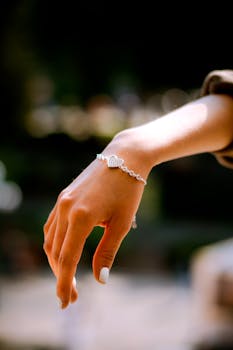 Close-up of a woman's hand wearing a heart charm bracelet outdoors, beautifully lit.