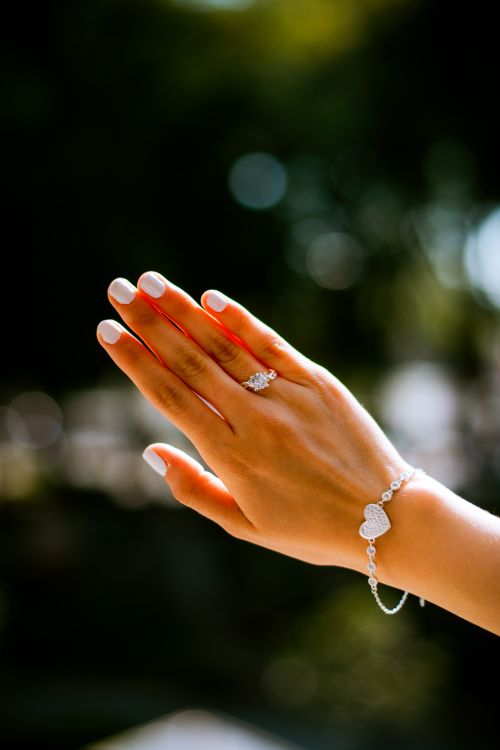 Free A close-up of a woman's hand adorned with a diamond ring and bracelet against an outdoor backdrop. Stock Photo