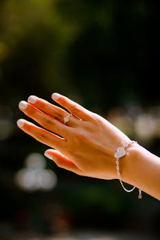 Close-up of a hand wearing a heart bracelet and ring, illuminated by sunlight with a soft bokeh background.