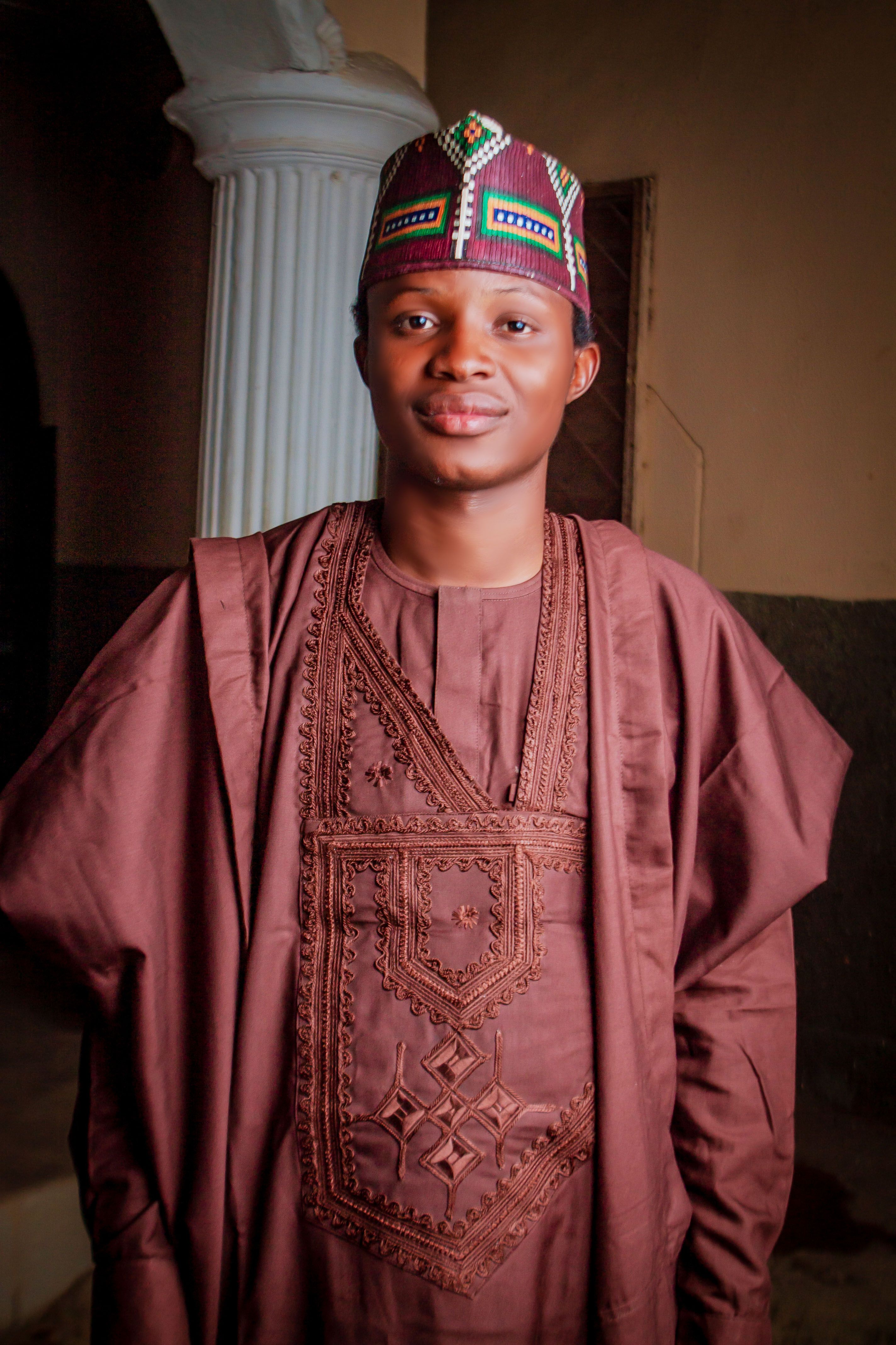 Portrait of a man wearing traditional African attire, standing indoors with a warm expression.