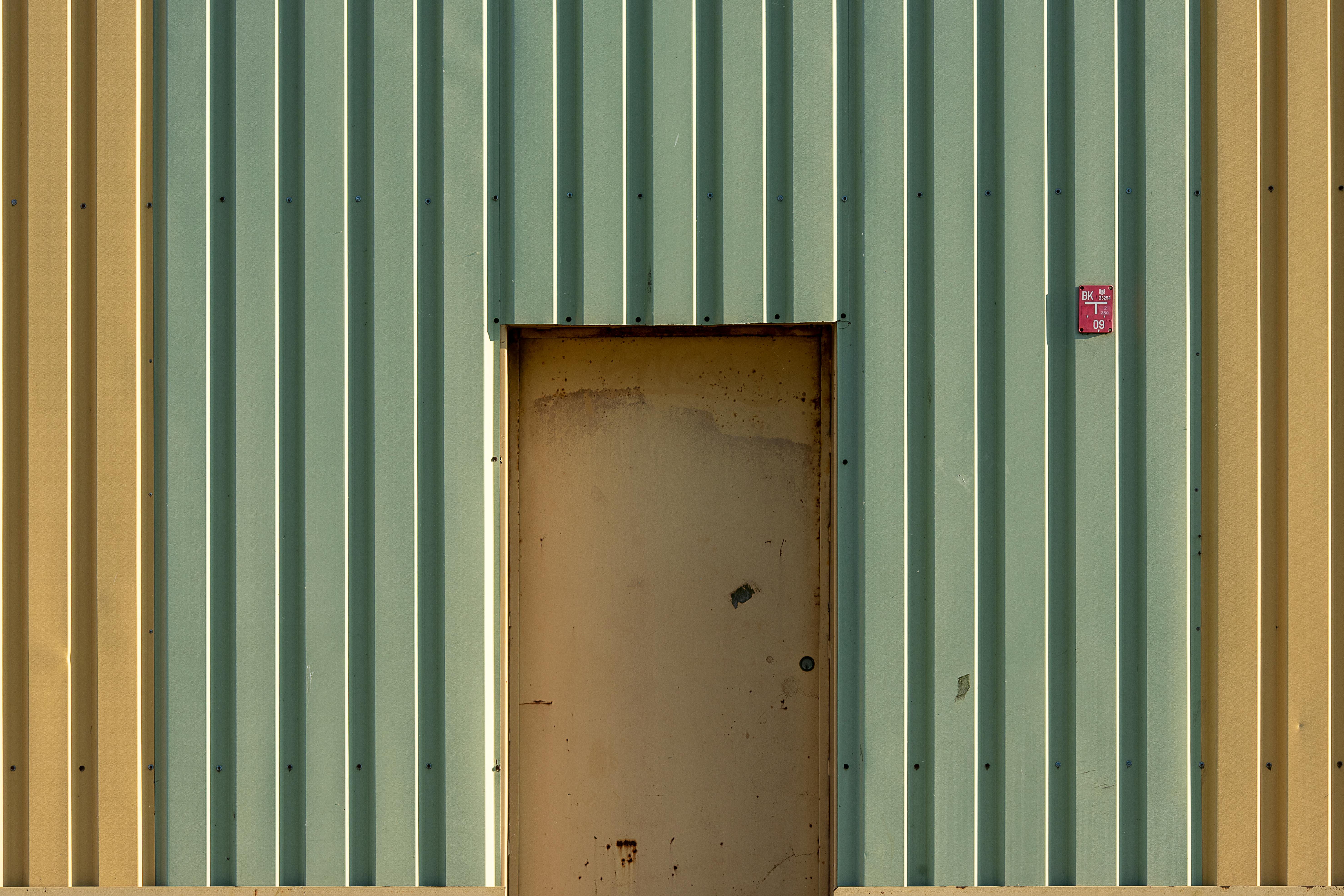 Gratis Una porta rustica in metallo inserita nella facciata di un edificio in acciaio ondulato con linee verticali. Foto a disposizione