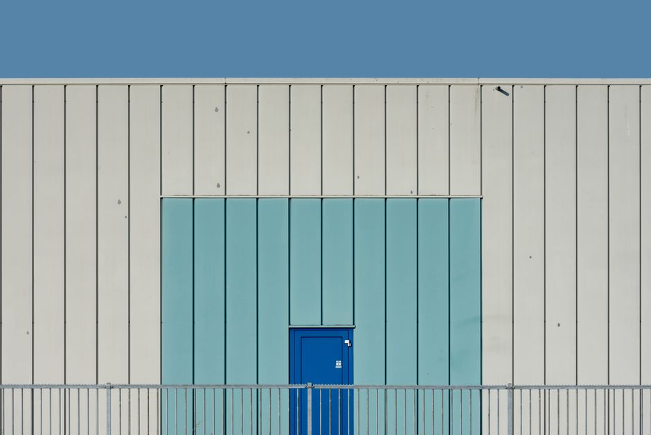 A minimalist modern building facade featuring a striking blue door against a pale blue and cream wall.
