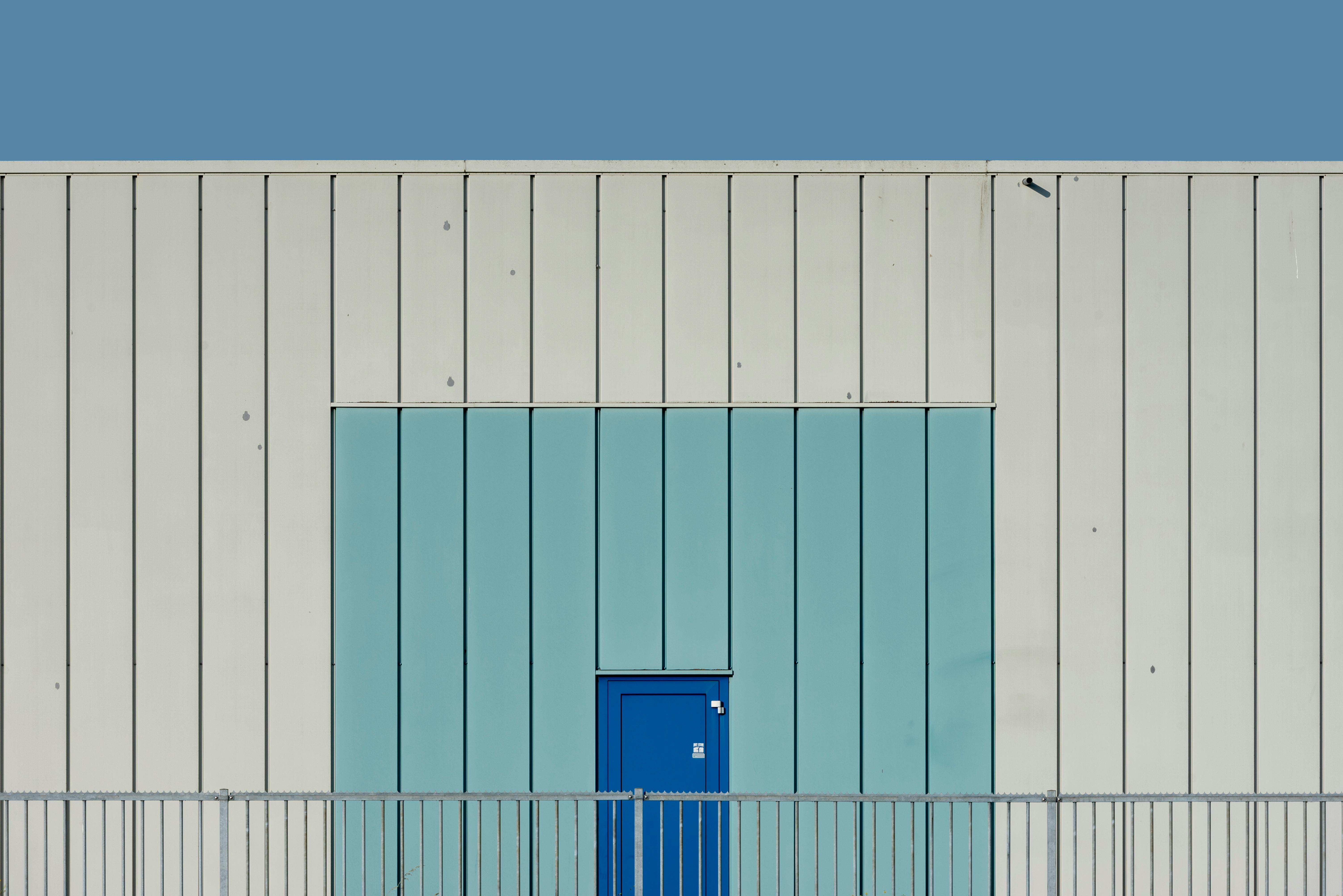 Zadarmo Minimalistická moderná fasáda budovy s výraznými modrými dverami na bledomodrej a krémovej stene. Fotka z fotobanky