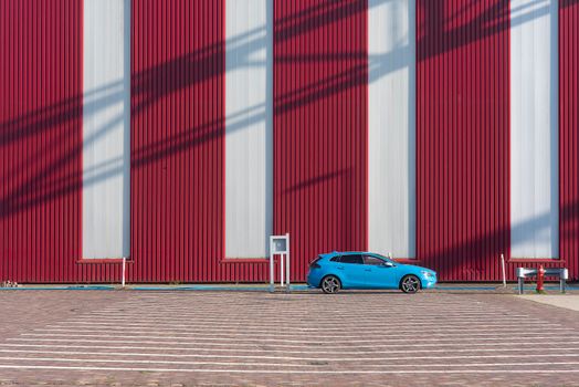 A vibrant blue car parked against a striking red wall in an empty parking lot, highlighting minimalist design.