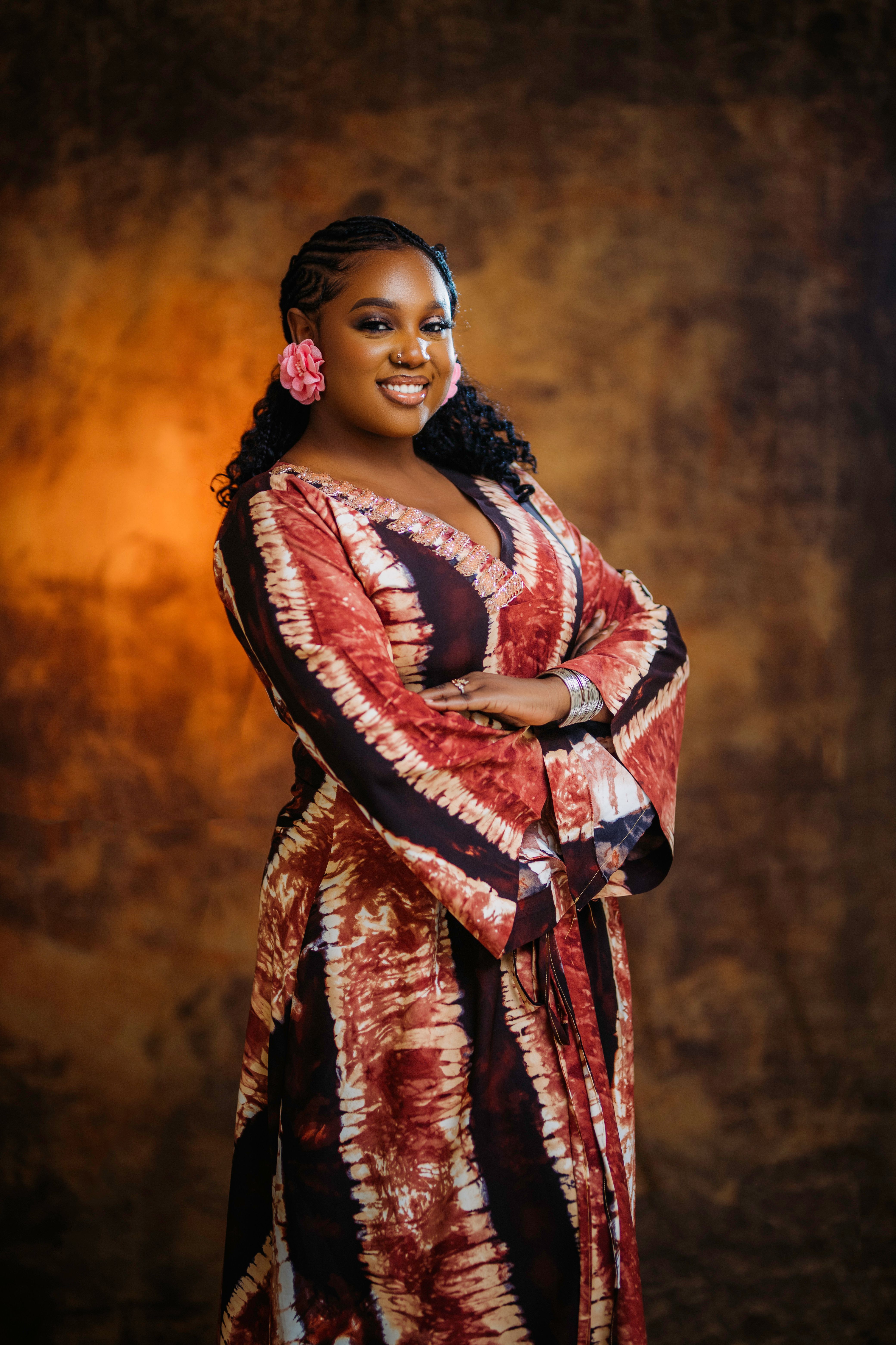 gratis Lachende vrouw in een levendige Afrikaanse jurk tegen een warme, gestructureerde achtergrond. Stockfoto