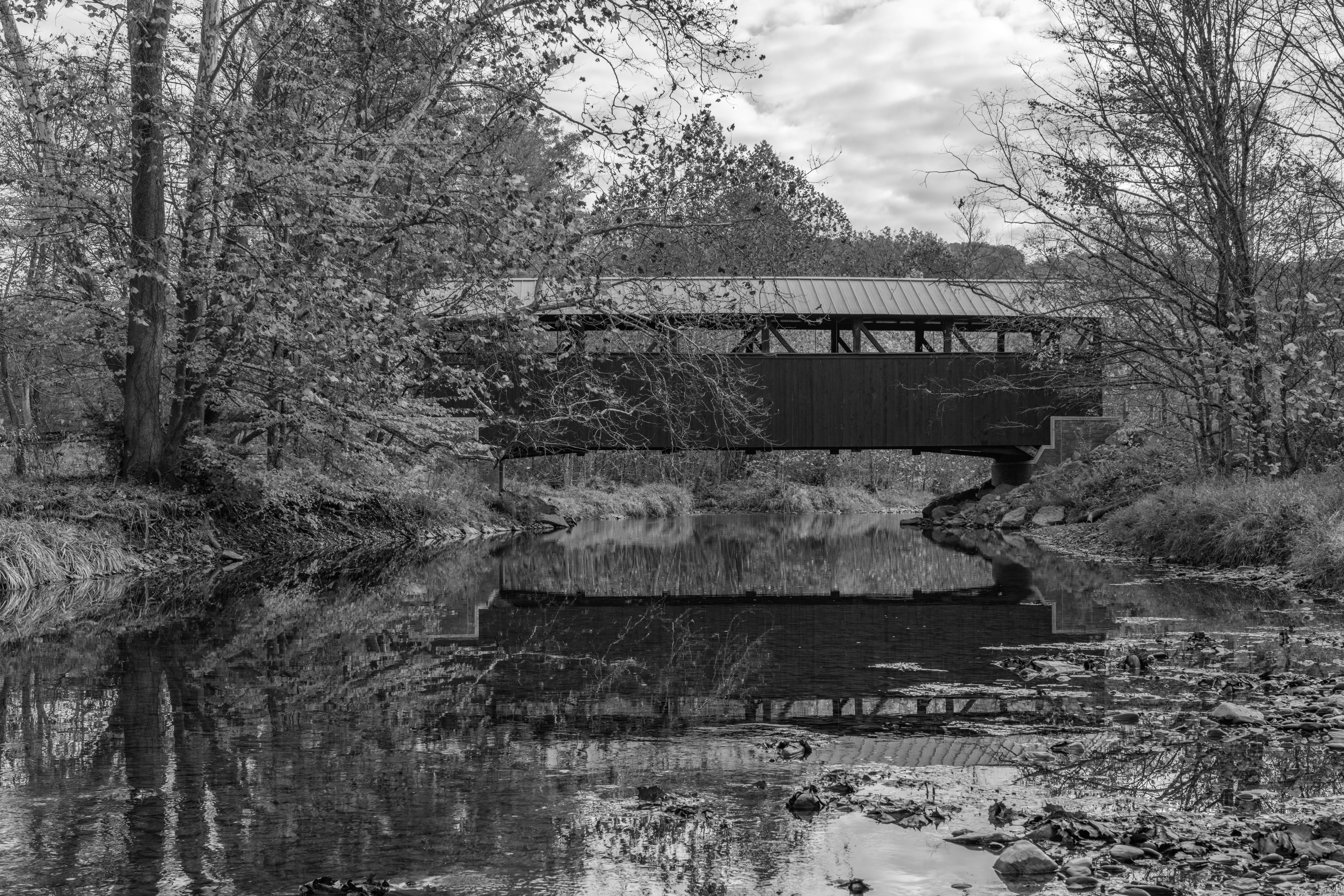 Black and white photo of a historic covered bridge over a serene river in Pennsylvania, USA.