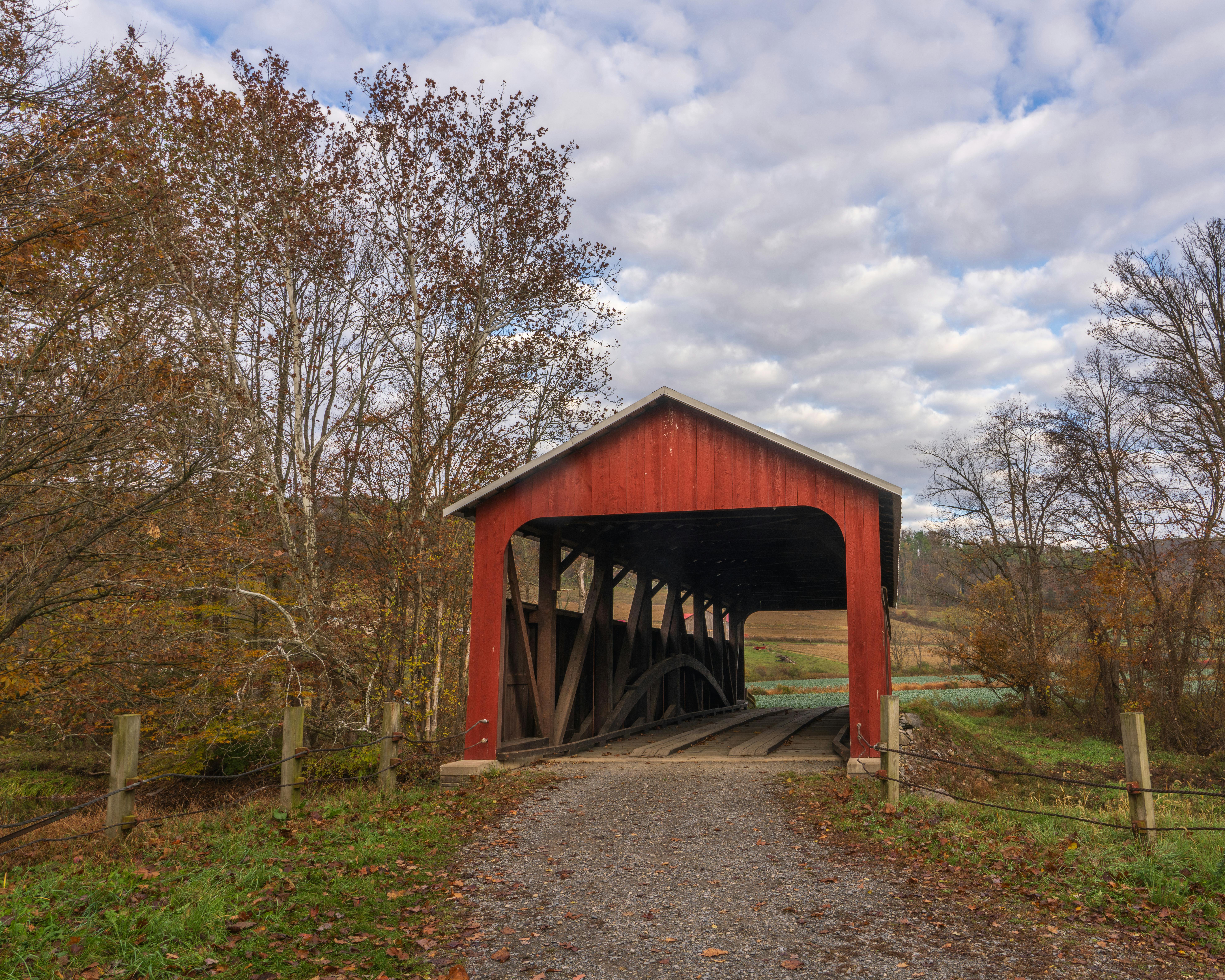 A charming red covered bridge in Pennsylvania during fall, surrounded by autumn foliage.