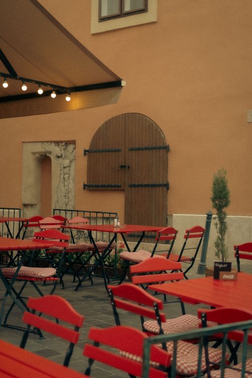 Free Captivating view of a cozy outdoor café setting featuring vibrant red tables and chairs. Stock Photo