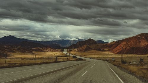 Free Empty highway through arid landscape with dramatic clouds and mountains. Stock Photo