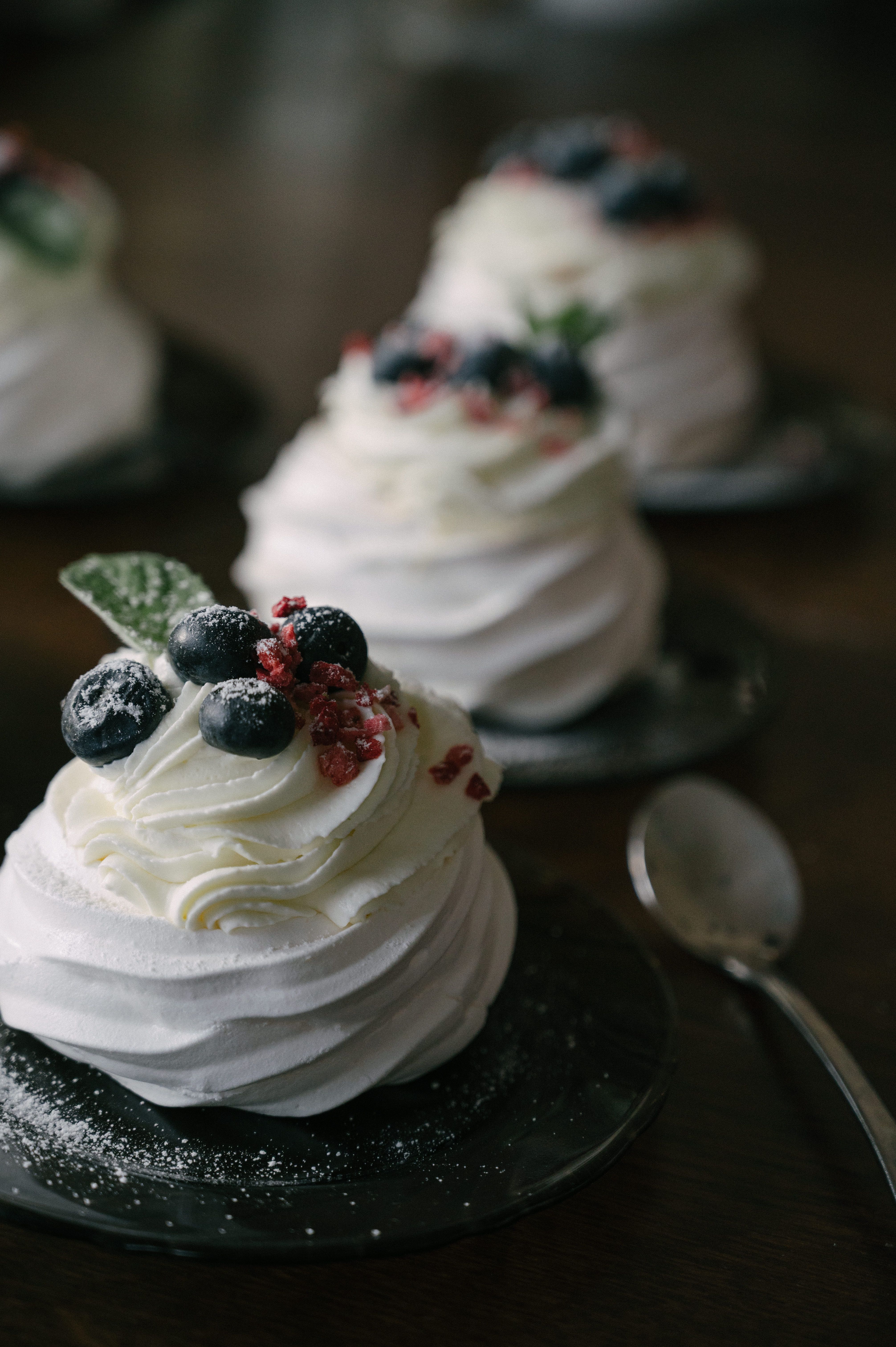 Delicious mini pavlova topped with blueberries and cream on a dark plate.