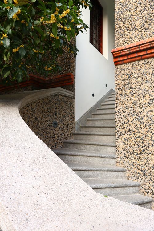 Free Elegant curved stone staircase leading to a residential entrance, surrounded by greenery. Stock Photo