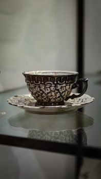 Detailed antique coffee cup and saucer with floral design on reflective surface indoors. — photo by Türker Burak TURGUT