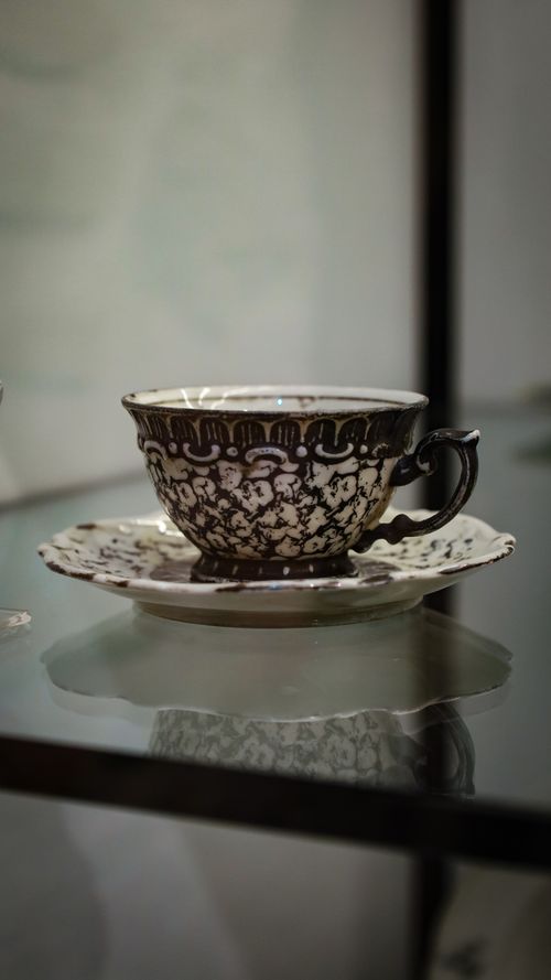 Free Detailed antique coffee cup and saucer with floral design on reflective surface indoors. Stock Photo